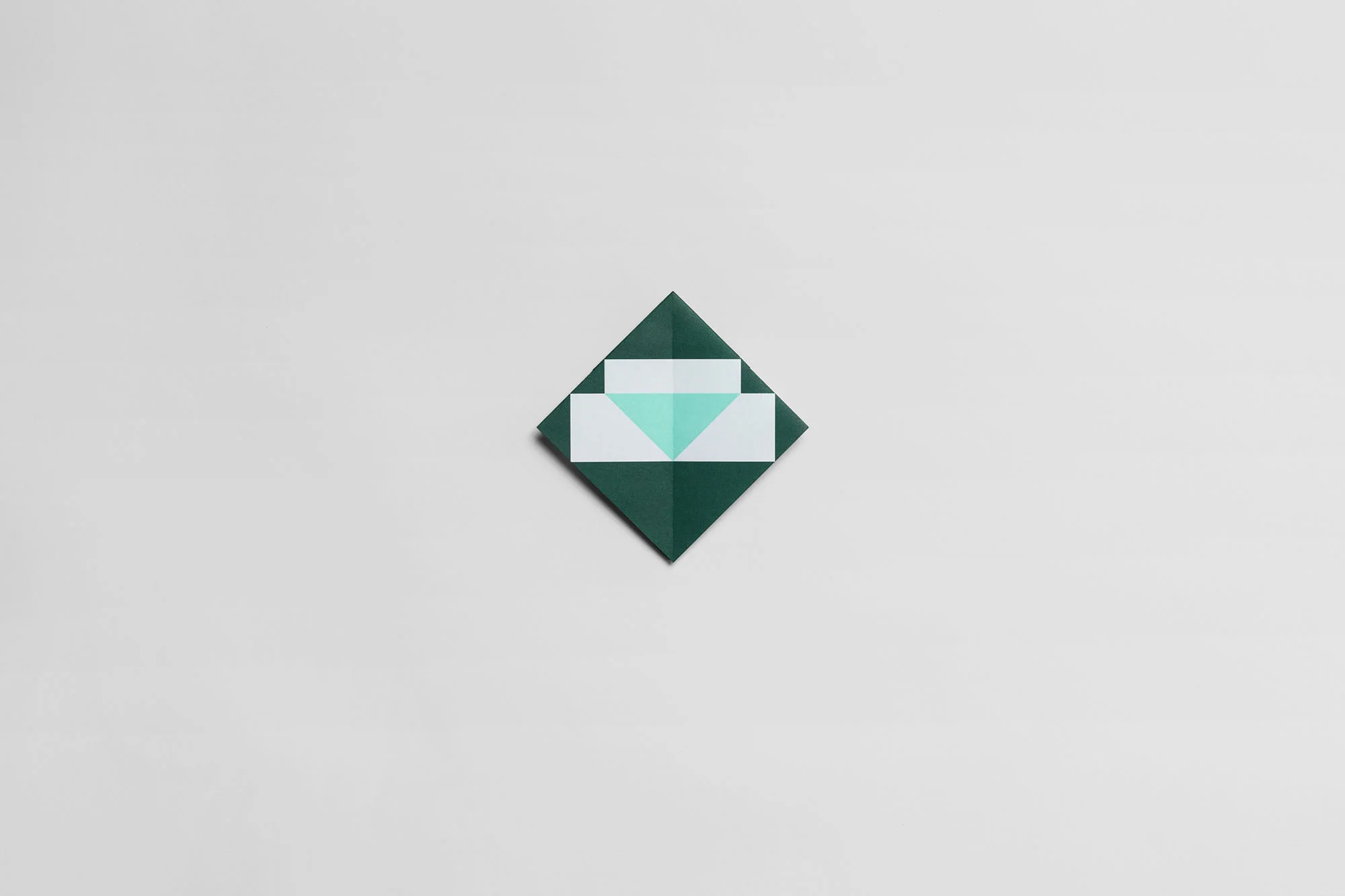 Overhead shot of an origami envelope with geometric shapes, folded with dark green and light green paper on a white background.