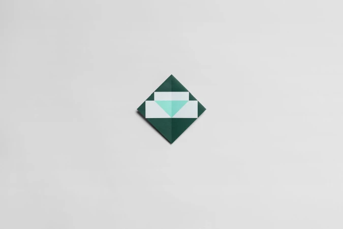 Overhead shot of an origami envelope with geometric shapes, folded with dark green and light green paper on a white background.