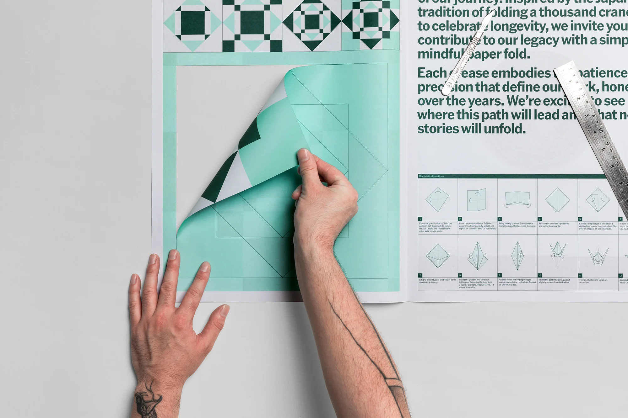 Close-up of a person peeling back a corner of a graphic print featuring geometric patterns and text instructions on paper folding.