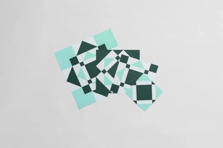 Three overlapping square geometric pattern cards in green, mint, and white on a plain grey seamless background.