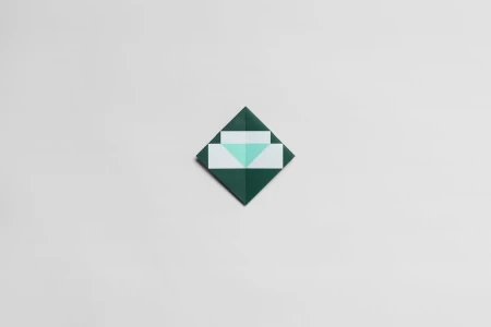 Folded geometric paper sculpture in dark green and white against a neutral light grey background.