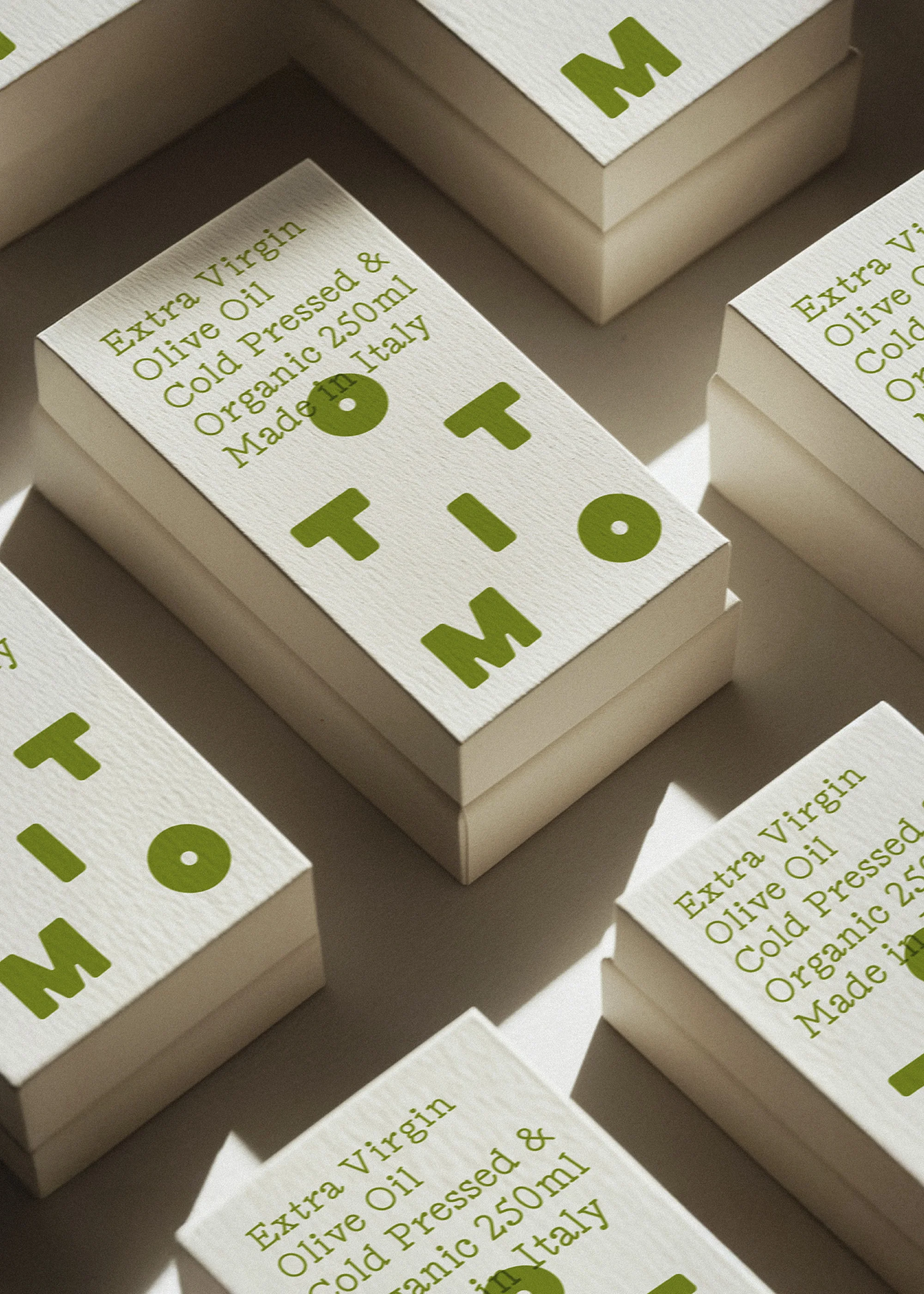 Close-up of olive oil product boxes arranged in a pattern. The boxes are printed with text and a company logo in green ink.