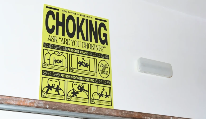 Informational poster on a white wall with step-by-step illustrations describing how to help someone who is choking, black text on yellow.