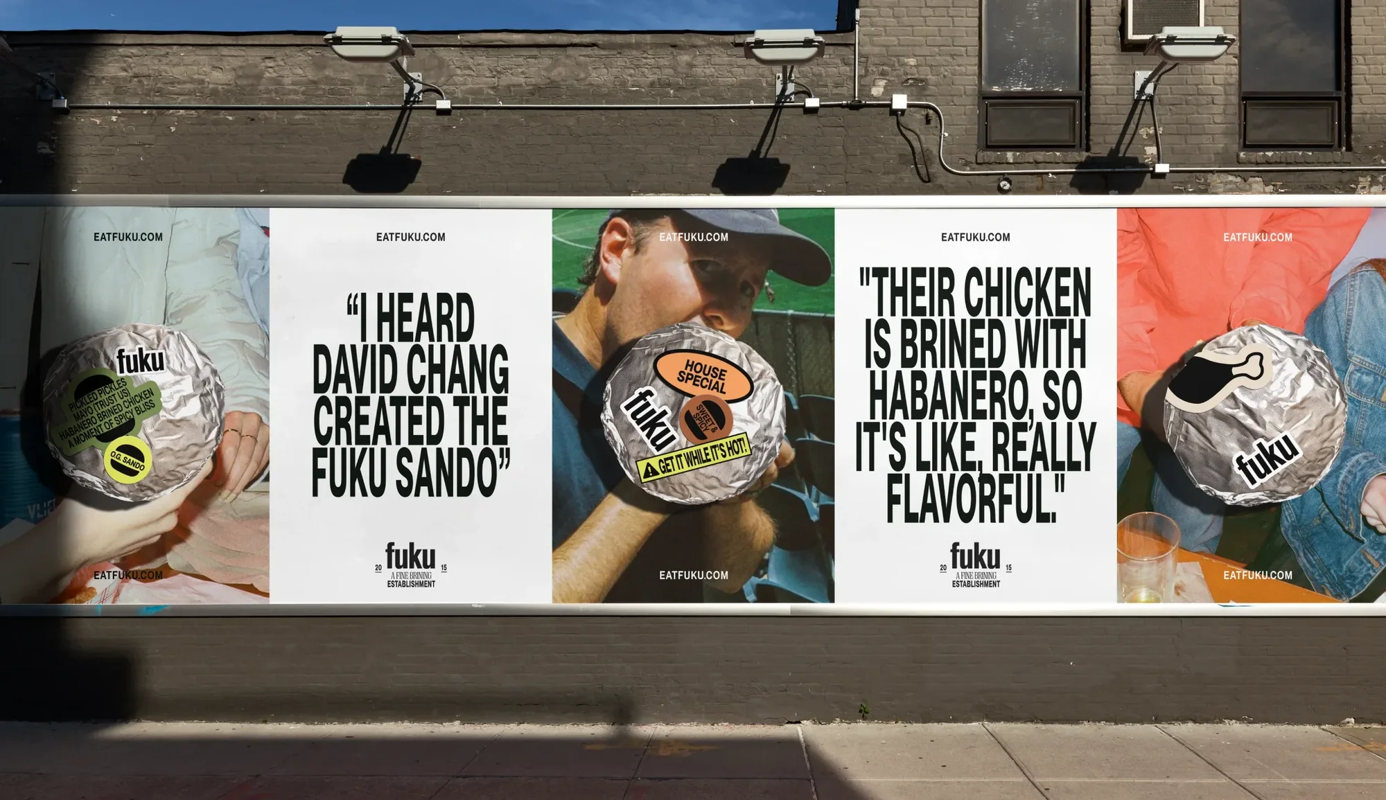 Fuku restaurant advertisement on a city street billboard features a sandwich wrapped in foil and bold text promoting their menu.