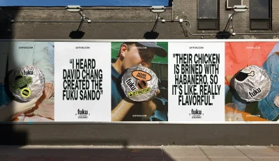 Fuku brand identity billboard on a dark brick wall featuring multiple vertical panels with bold typography and foil-wrapped sandwiches