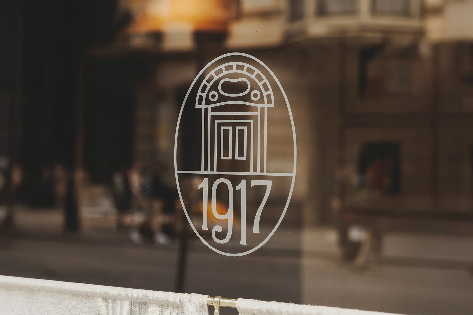 Illuminated logo on glass features a door with the number 1917. An interior scene is visible through the glass, creating depth and texture.