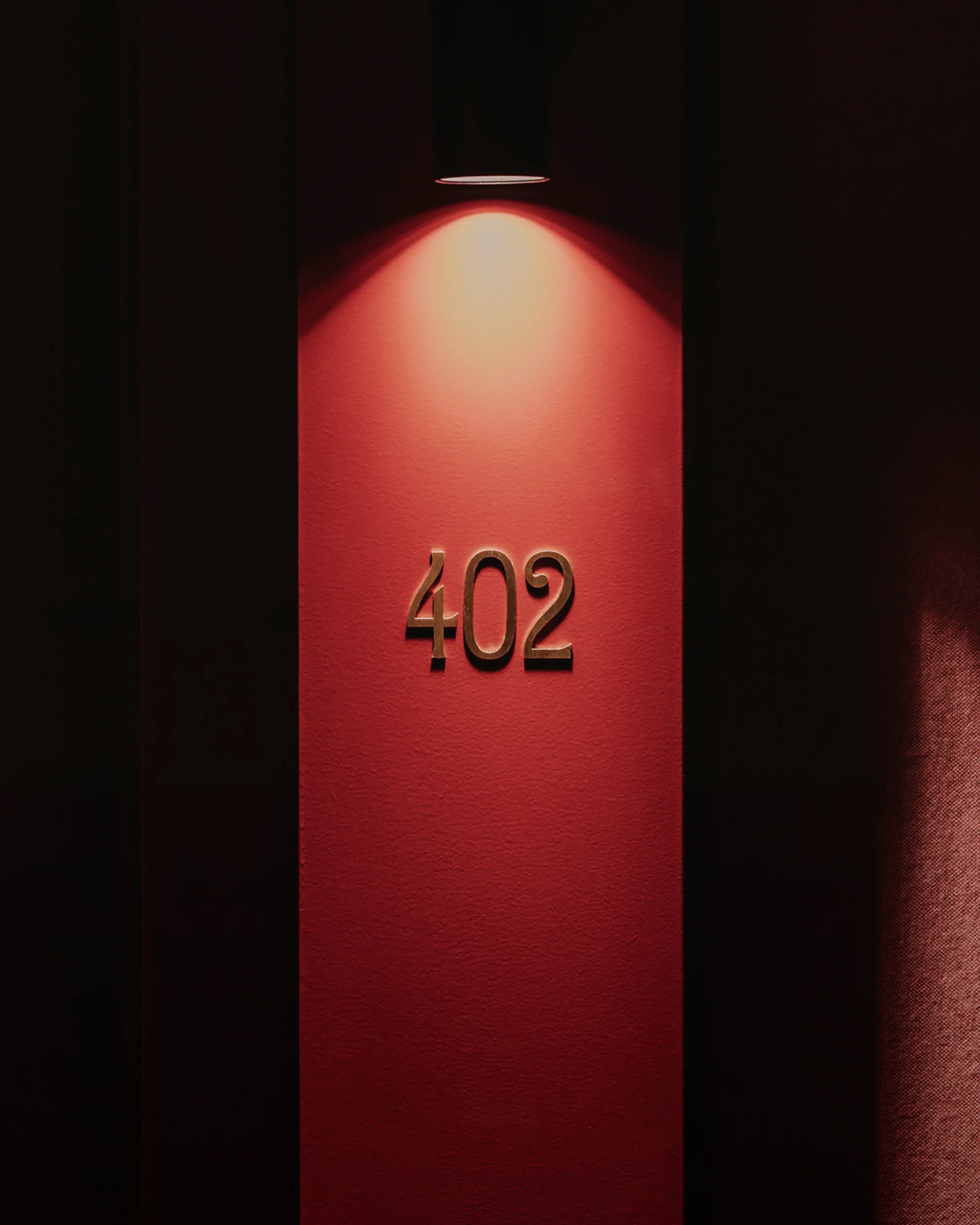 Illuminated room number 402 mounted on a red wall in a dimly lit hallway creates a sense of mystery and anticipation for the guest.