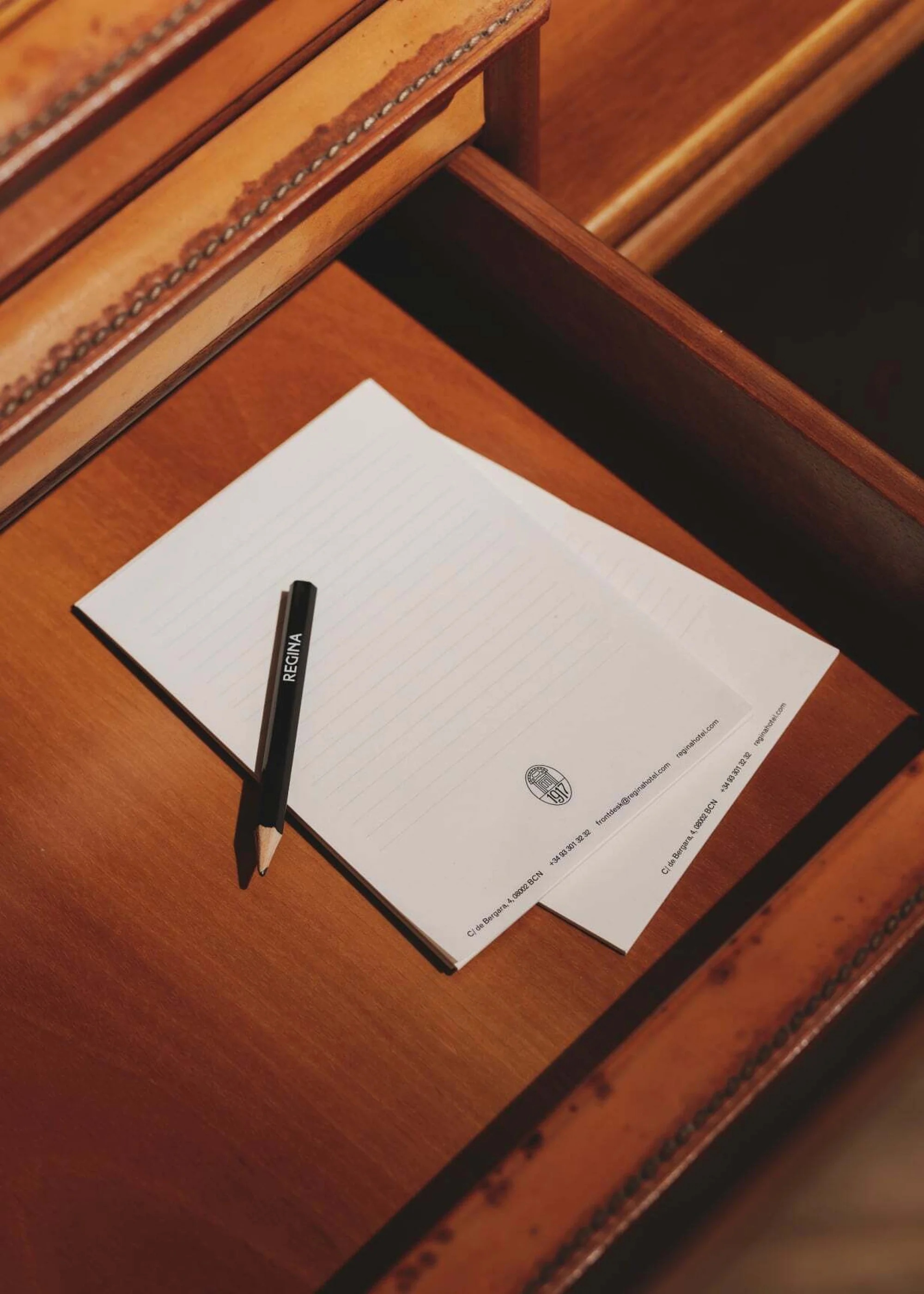 Close-up of two sheets of paper with 'Regina' pen on a wooden desk with a leather-trimmed drawer, capturing a scene of refined elegance.