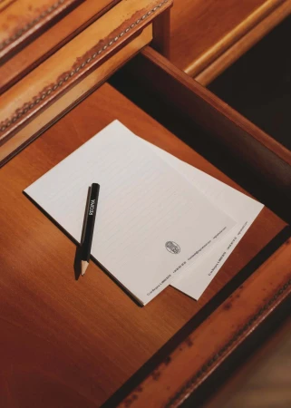 Close-up of two sheets of paper with 'Regina' pen on a wooden desk with a leather-trimmed drawer, capturing a scene of refined elegance.