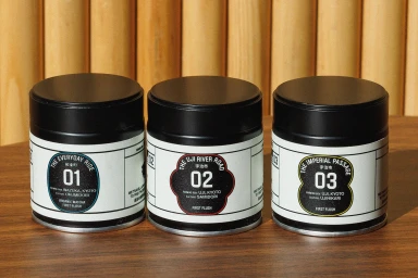 Three black cylindrical matcha tea tins with white labels numbered 01, 02, and 03 arranged on a wooden table.