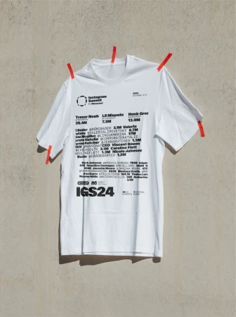 A white T-shirt, pinned to a light grey wall, features an Instagram Summit graphic with names like Trevor Noah and Lil Miqueli.