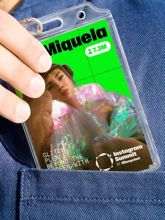 Hand holding a name badge with a woman's photo on a bright green background. The badge is tucked into a blue denim pocket.