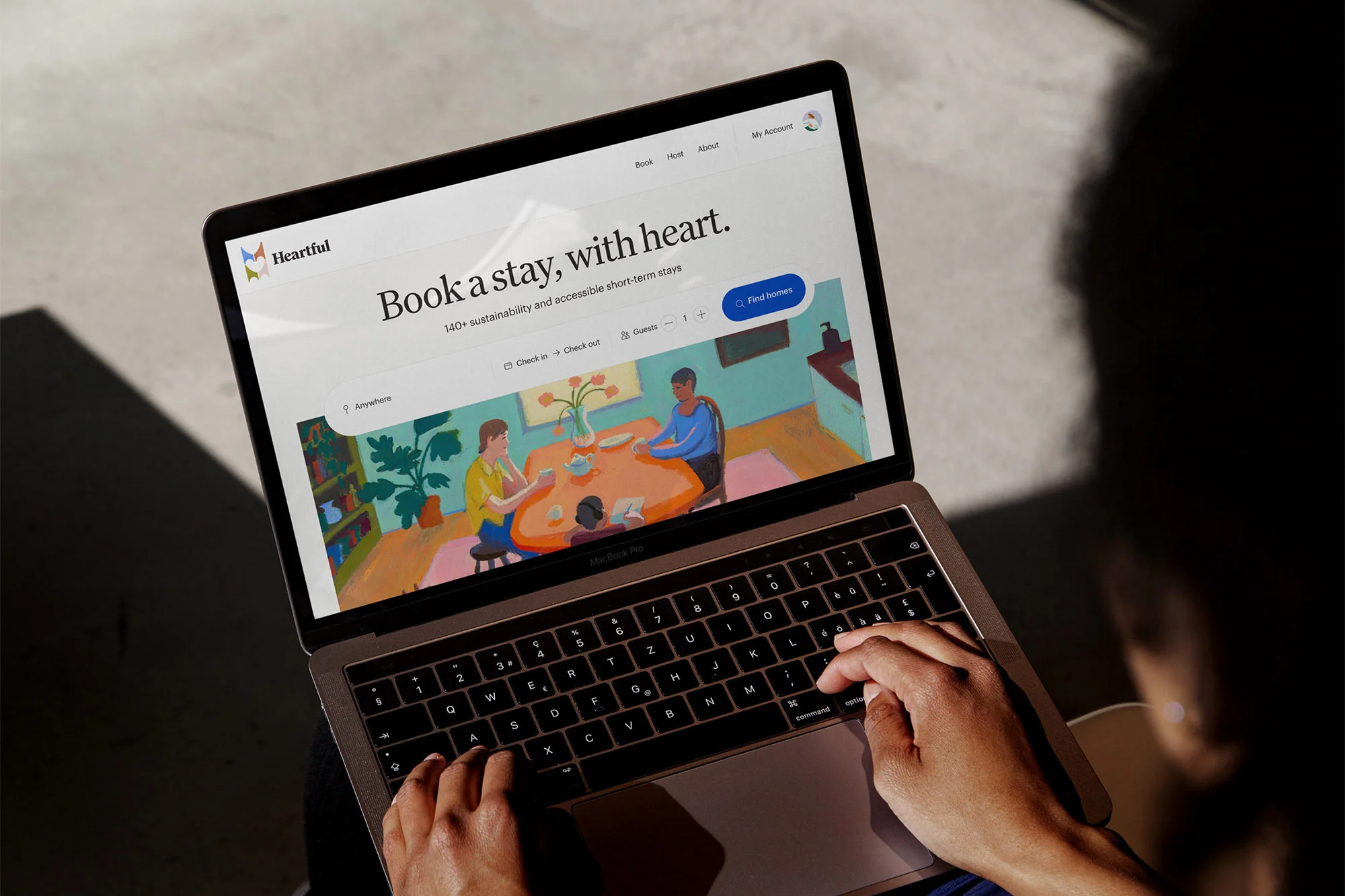 Person types on a laptop with the Heartful website, featuring an illustration of people at a table. Warm lighting. Home interior setting.