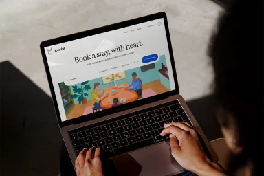Close-up over-the-shoulder shot of hands typing on a laptop displaying the Heartful brand identity website interface.