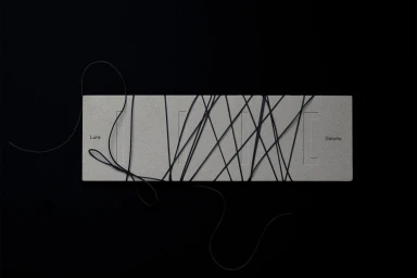 Grey cardboard brand identity piece for Lure wrapped in black string against a solid black background.
