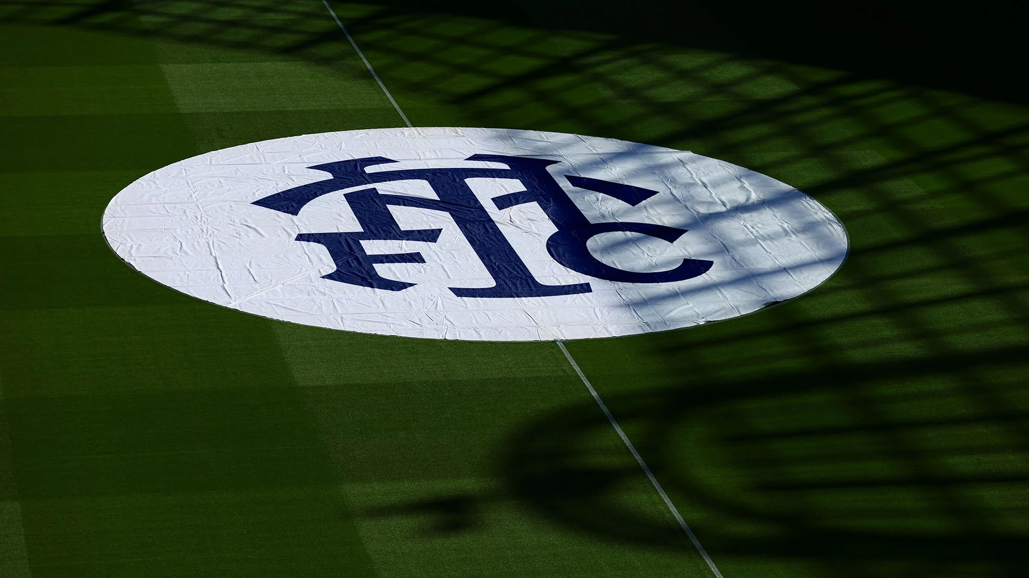 Overhead shot of a sports field with a large white oval shape featuring a dark blue logo in the center, creating a focal point.