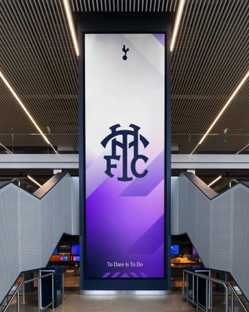 Tottenham Hotspur Football Club stadium signage with their logo and motto, 'To Dare Is To Do,' visible indoors.