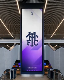 Large vertical Tottenham Hotspur brand identity banner displayed in a modern building atrium between staircases