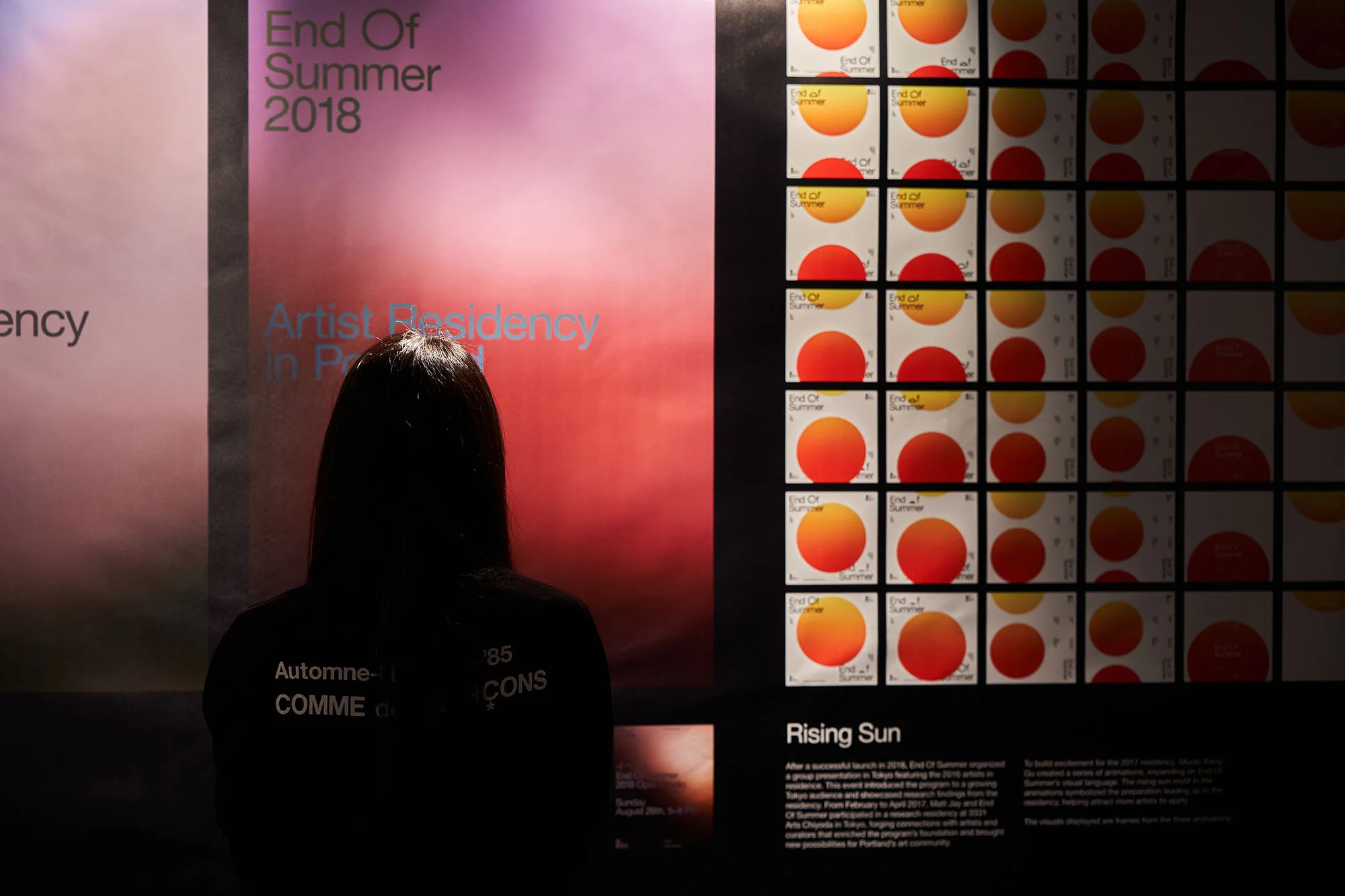 Back view of person looking at wall art posters featuring rising sun graphics and text, in an indoor setting with diffused lighting.