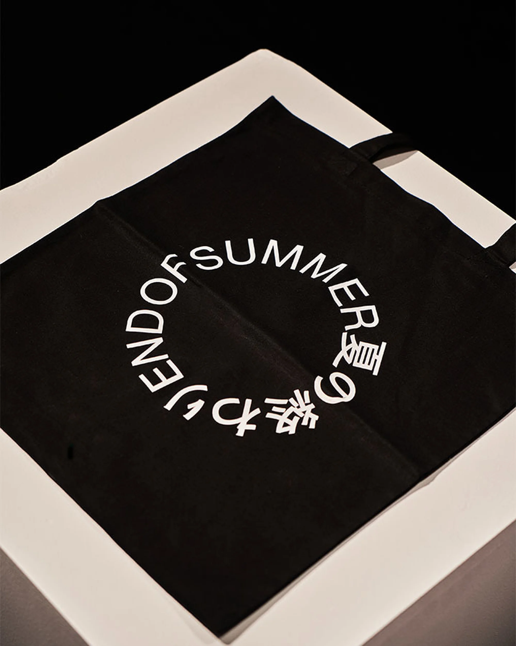 Black canvas tote bag with circular white typography resting on a white display surface
