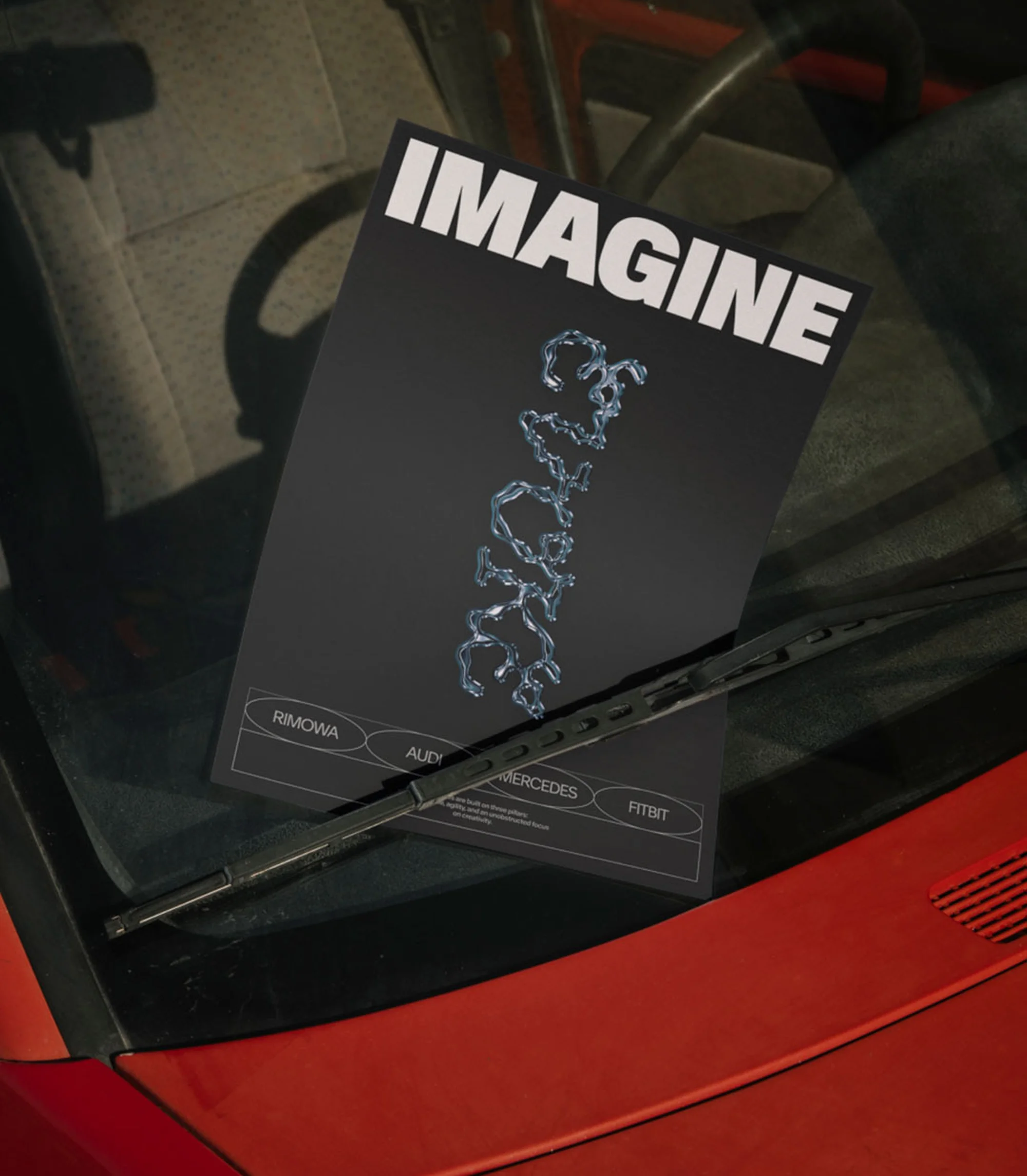 Promotional material featuring 'Imagine' design displayed on car windshield with wiper blades and car interior visible in shot.