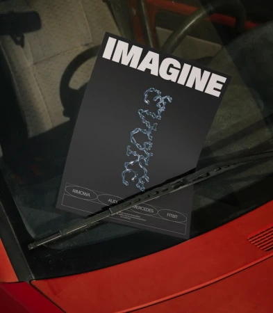 Promotional material featuring 'Imagine' design displayed on car windshield with wiper blades and car interior visible in shot.