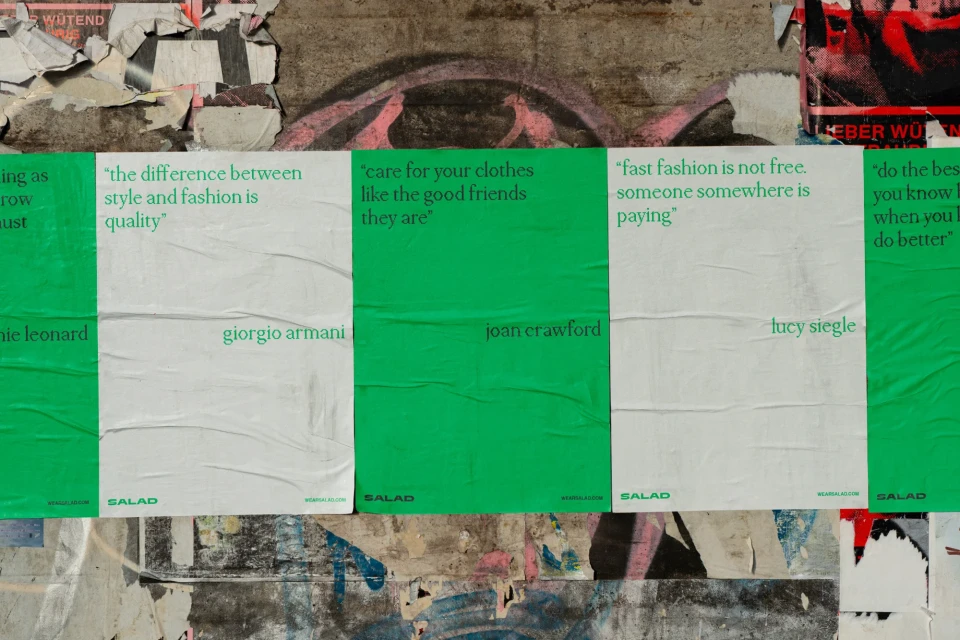 Posters with fashion quotes by Annie Leonard, Giorgio Armani, Joan Crawford, and Lucy Siegle on a weathered wall.