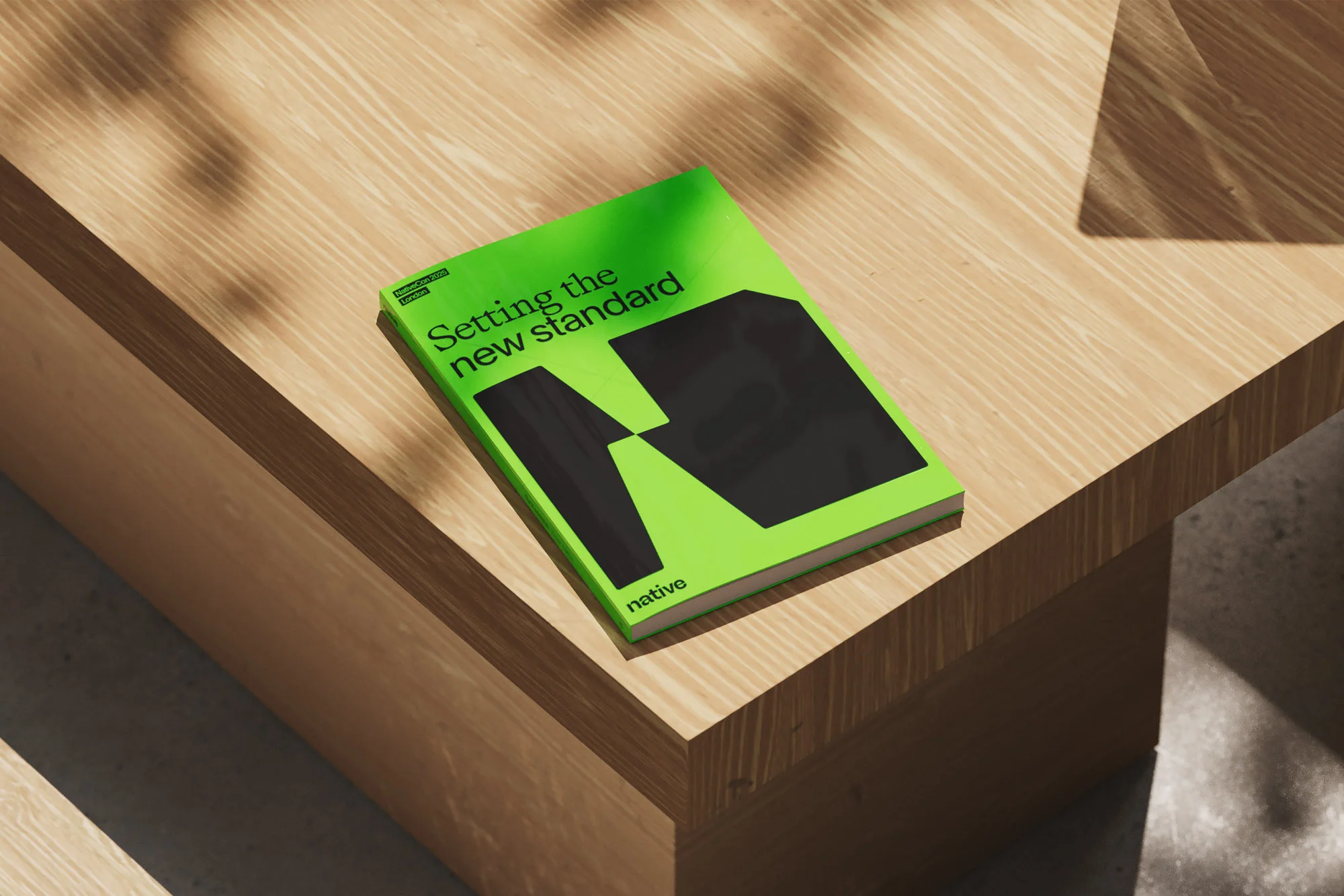 Close-up of a bright green book titled 'Setting the New Standard' with black geometric shapes on a light wood table.