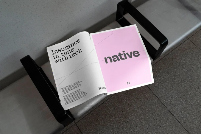 Open magazine with a pink page and the word 'native' in gray letters resting on a metal bench seat indoors.