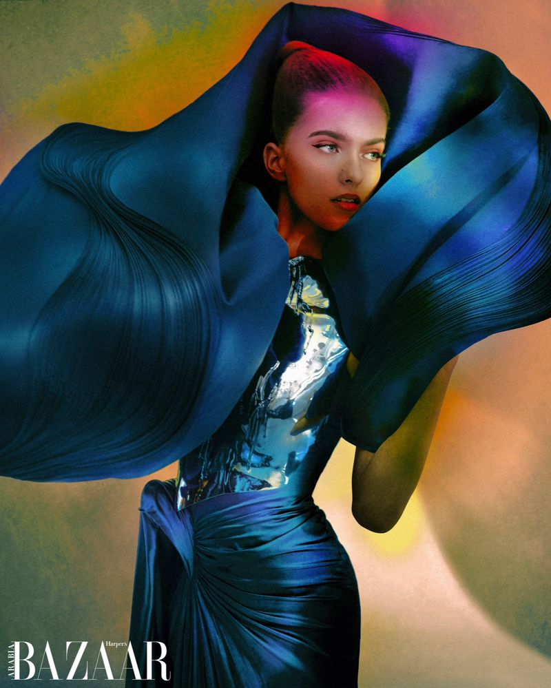 Fashion shot of a woman wearing a blue dress with oversized sculptural fabric around the head against a gradient colorful background.