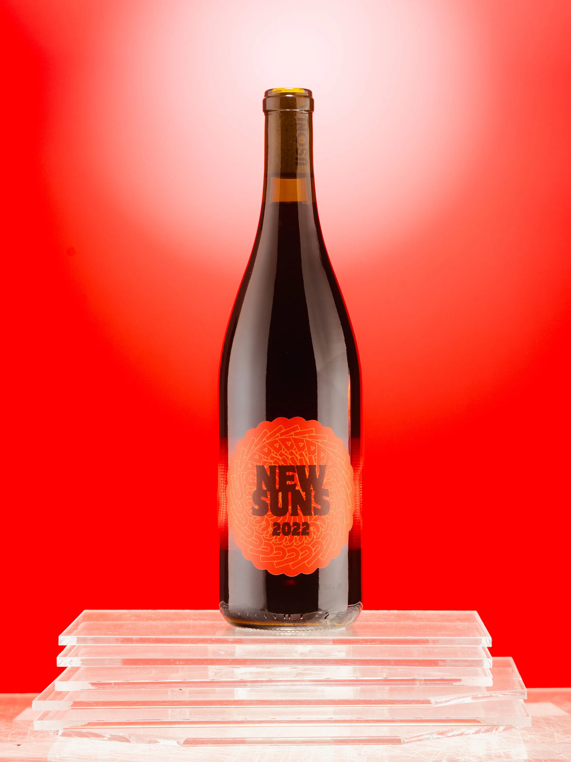 Wine bottle on stacked clear blocks against a vibrant red backdrop, featuring the 'New Suns 2022' label.