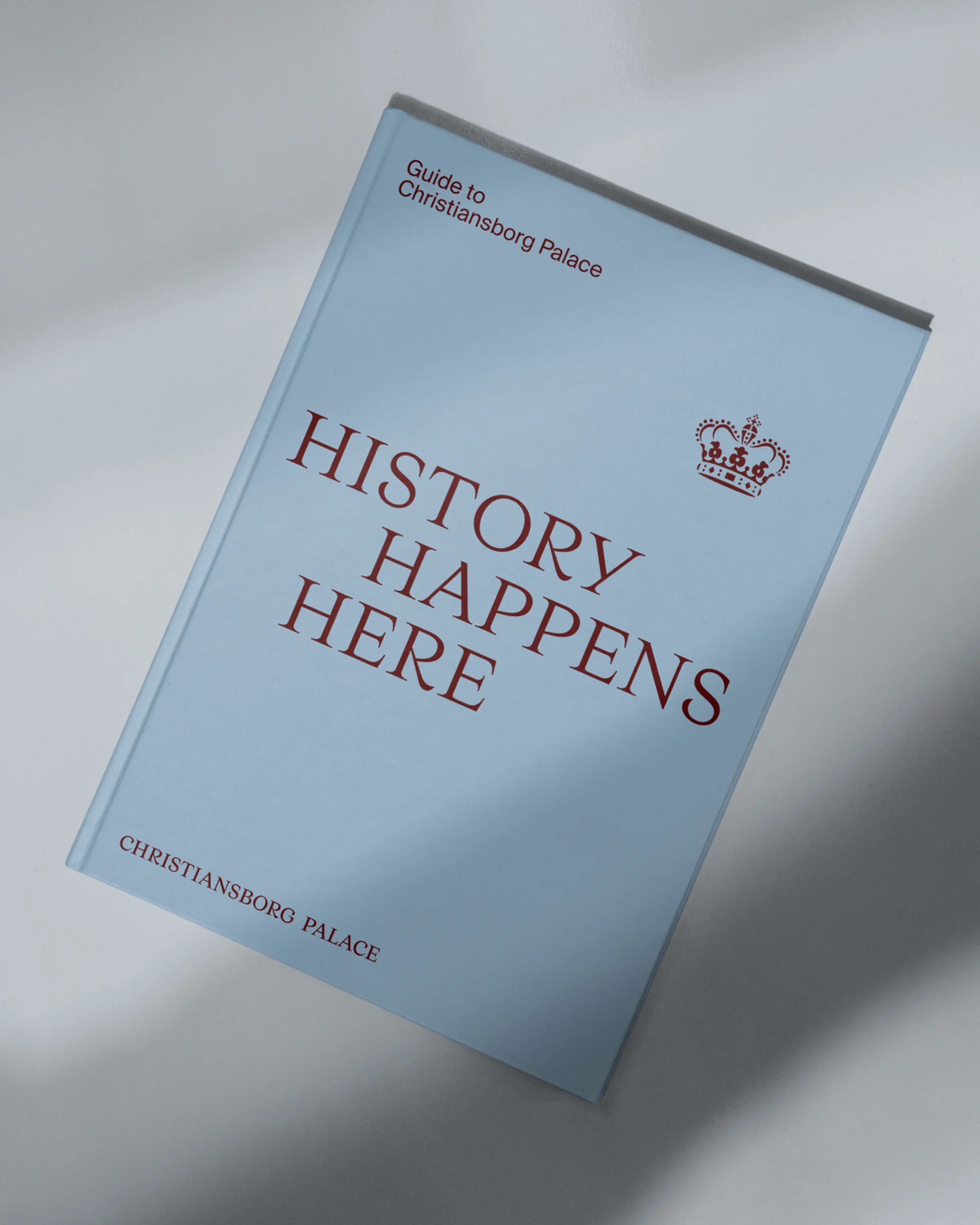 A light blue book titled 'History Happens Here' with a crown illustration, referencing Christiansborg Palace, is isolated on a white surface.