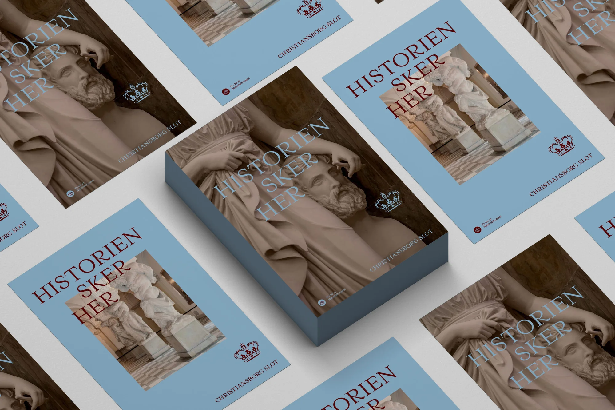 Stack of books with 'Historien Sker Her' cover, featuring classical statue art, against a pale blue background.