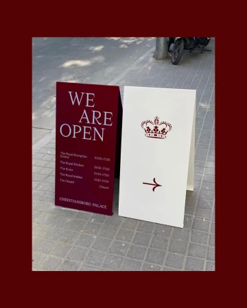 Two sandwich boards on a sidewalk: One advertises that 'We are Open,' and the other features a graphic of the Danish Crown.