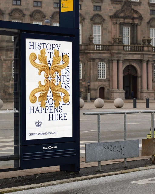 Outdoor advertisement in an urban setting showcases ornate gold flourishes and blue text for Christiansborg Palace on a bus stop.