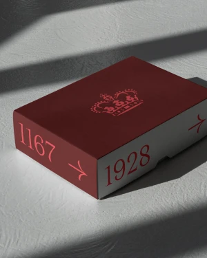 A burgundy and white rectangular box with printed crown emblem and numbers rests on a textured surface under directional light.