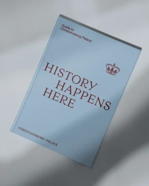 A light blue hardcover book titled Christiansborg Palace resting on a pale neutral surface with soft shadows
