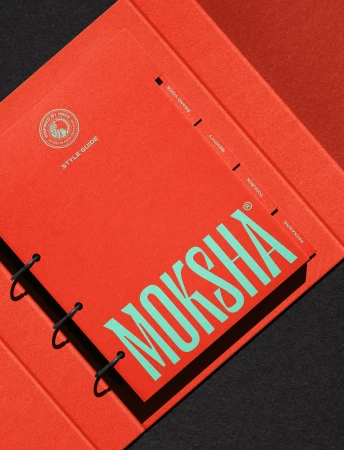 Open coral-colored folder with a ring-bound style guide on a black surface featuring the brand name MOKSHA in teal lettering.