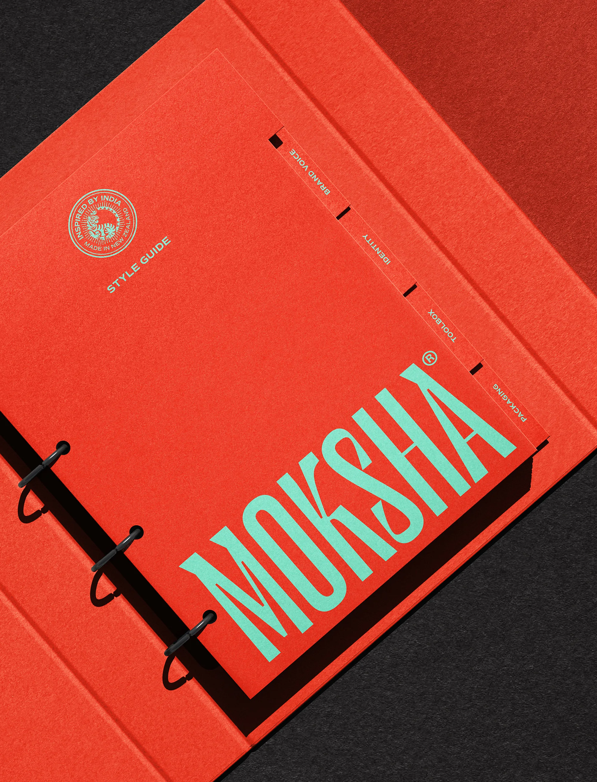 Red brand identity style guide ring binder featuring turquoise Moksha typography inside a matching red presentation box