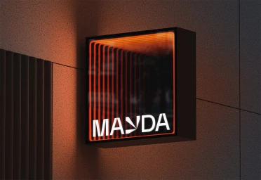 Square illuminated storefront sign featuring the Mayda brand name with an orange tunnel light effect mounted on a textured concrete wall.