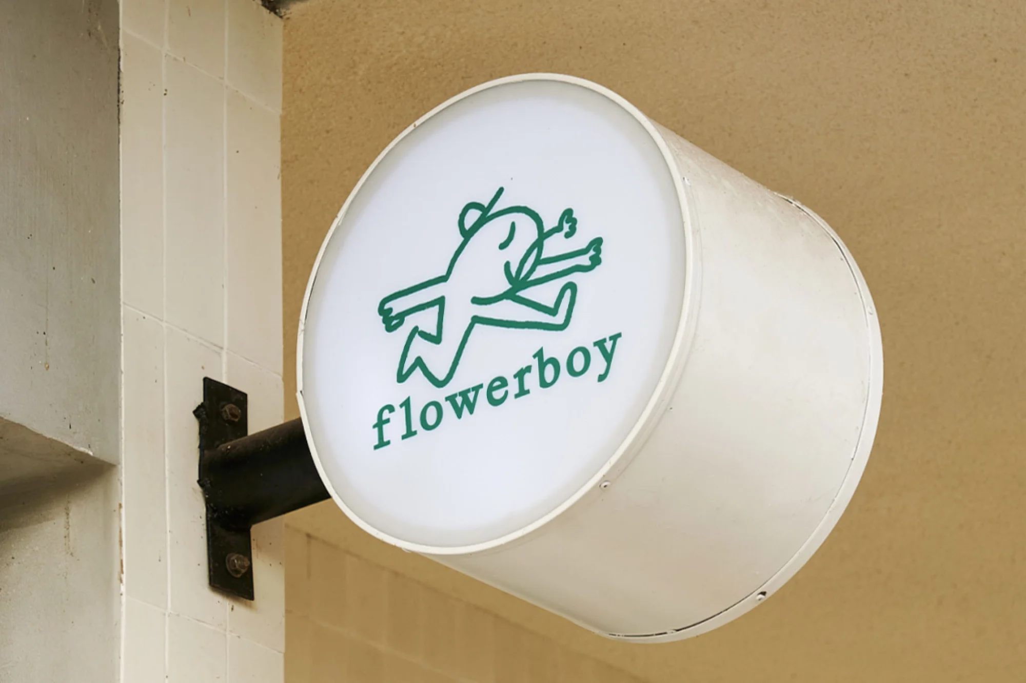 Circular lit sign for 'flowerboy' with a green cartoon figure outside a building, promoting a florist or plant shop.