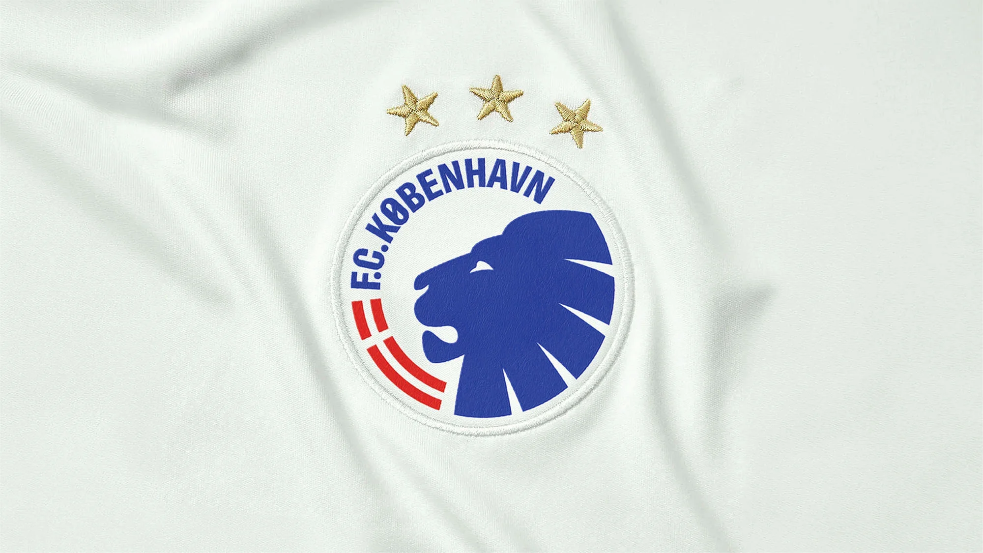Close-up of a white jersey with the F.C. Kobenhavn logo featuring a blue lion, red and white accents, and three gold stars.