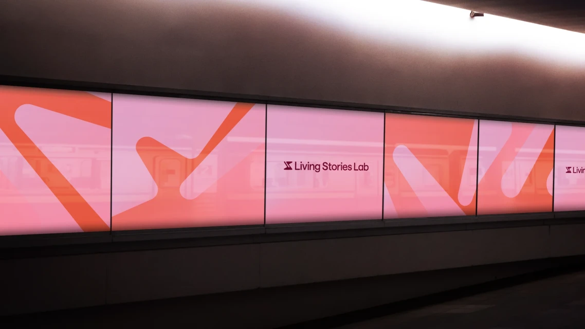 Large backlit wall graphic features pink and orange abstract design elements, along with 'Living Stories Lab' logo, illuminating the space.