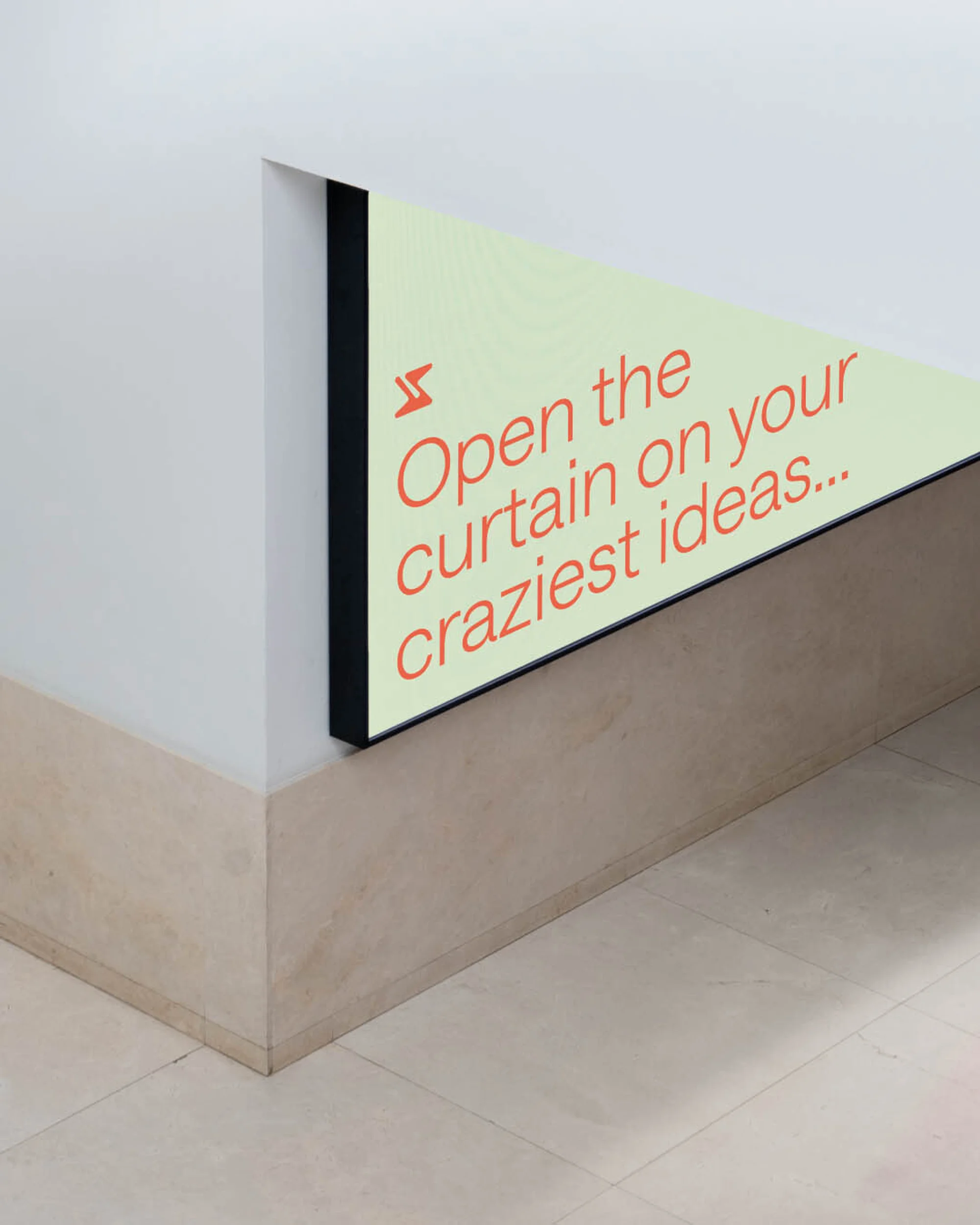 An interior wall featuring an illuminated, triangular sign with the text 'Open the curtain on your craziest ideas' in orange lettering.