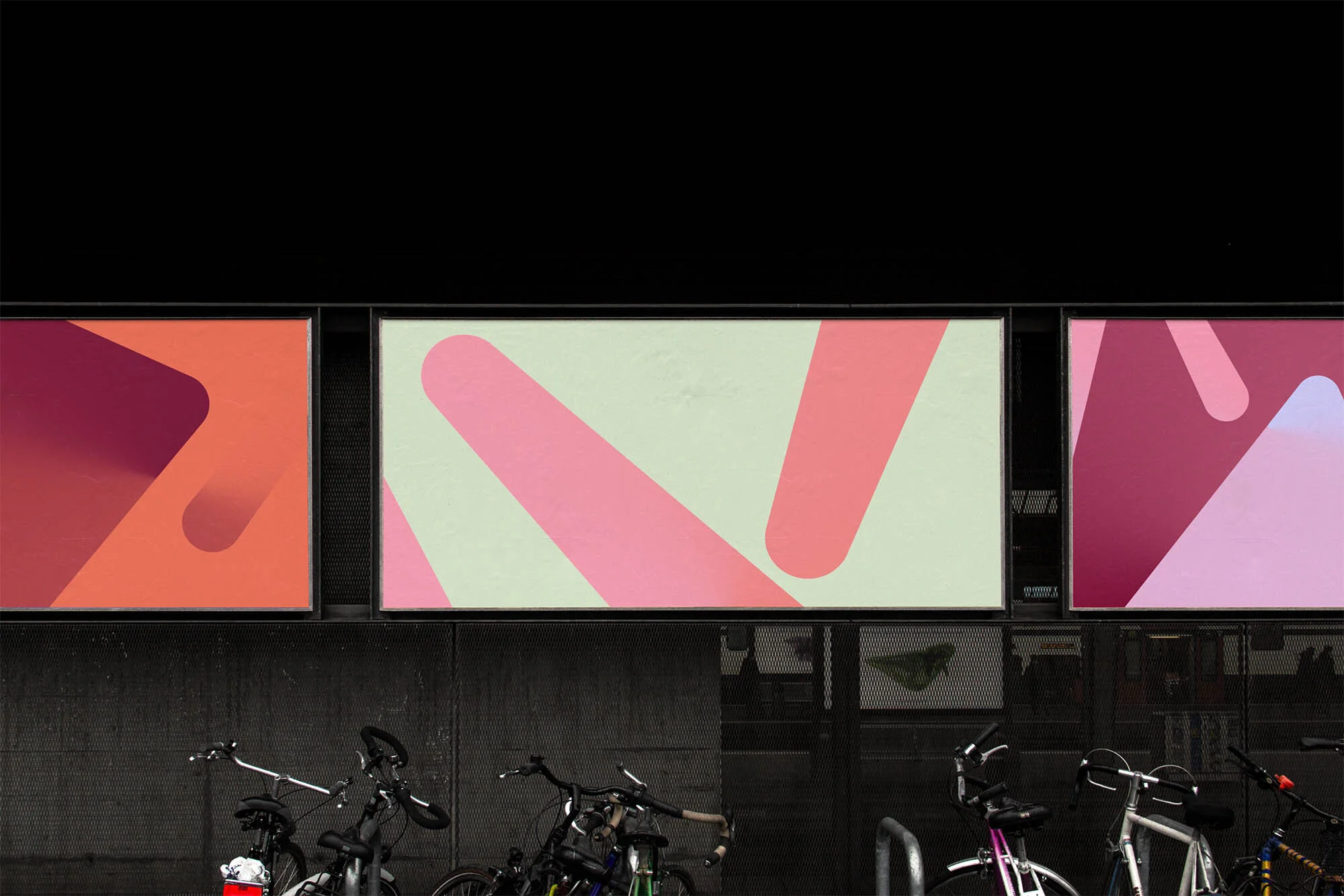 Three abstract art panels hang above parked bicycles. The panels feature graphic shapes in shades of pink and orange against a dark background.