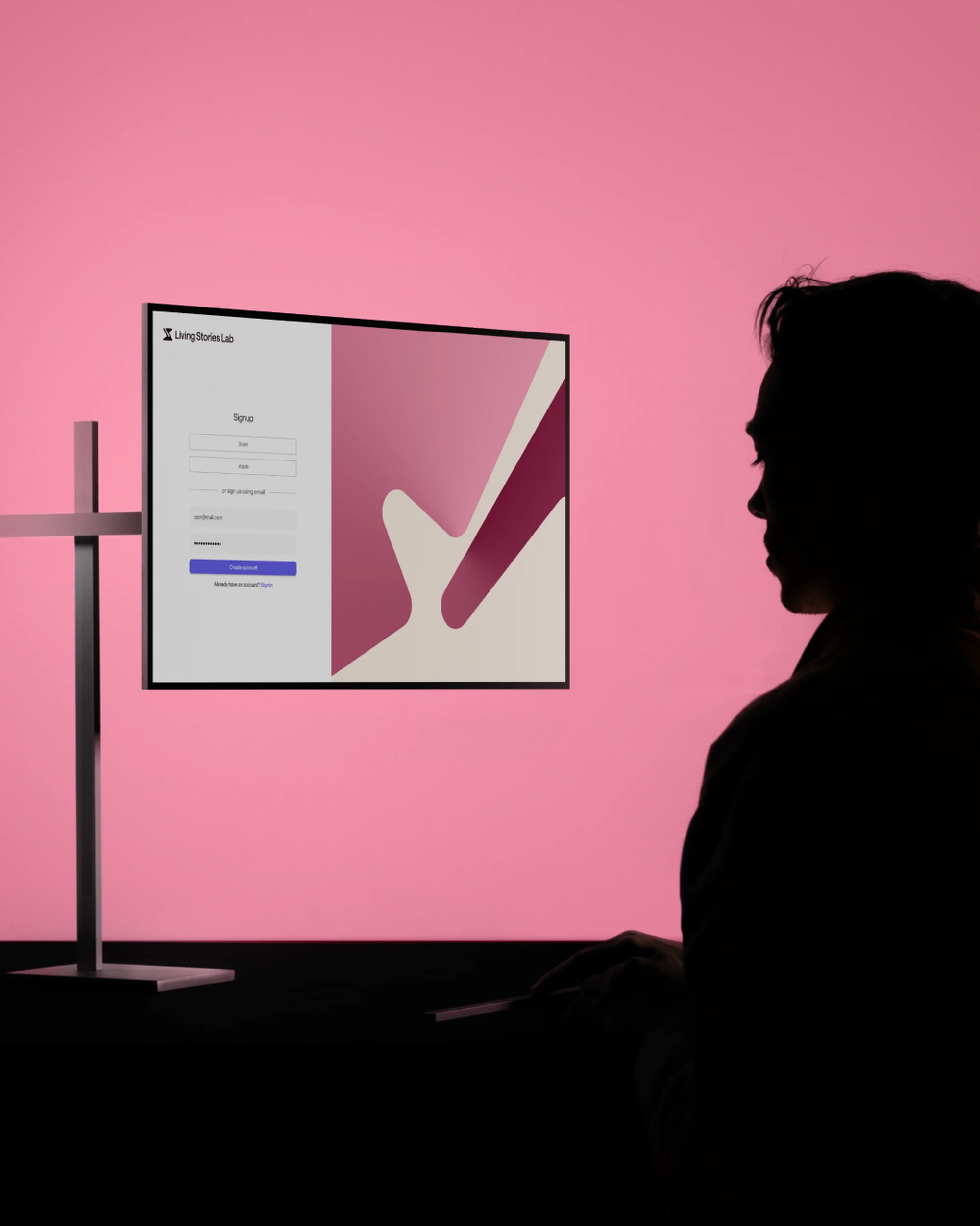 Silhouette of a person using a computer with a pink screen displaying login information and geometric shapes in a softly lit room.
