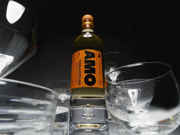 Tequila reposado bottle surrounded by empty wine glasses on a dark grey background, product shot with commercial appeal, liquor.