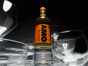 Amo Tequila Reposado bottle centered among multiple clear glass vessels against a dark background
