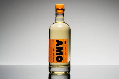 Amo Tequila reposado bottle with an orange label against a neutral grey seamless backdrop.