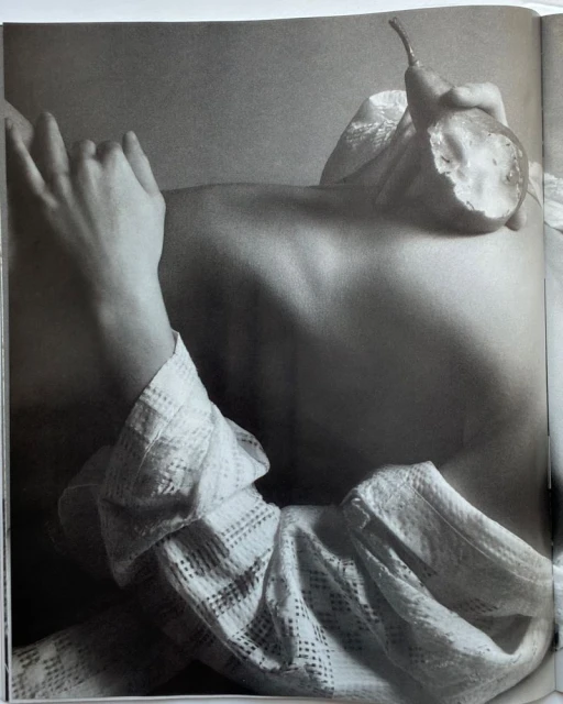 Monochrome upper body shot of a woman with her hands and a halved pear, highlighting body positivity and artistic still life in the studio.